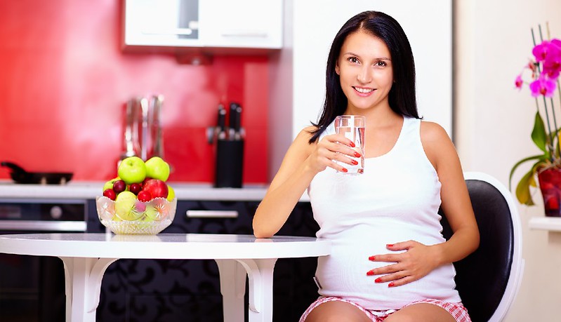 pregnant woman drinking water in kitchen